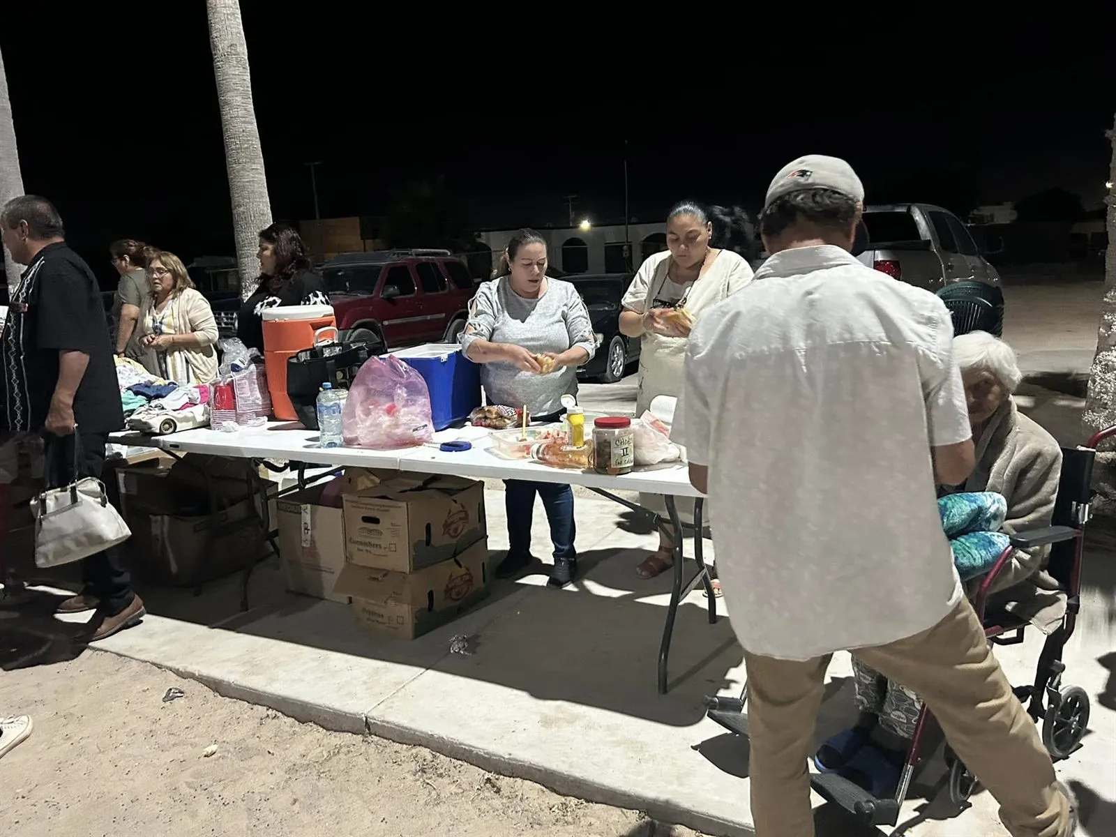 Volunteers handing out clothing and food from tables at an evening giveaway in Rocky Point, Mexico